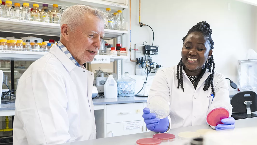 Two people wearing white lab coats sit in a lab.