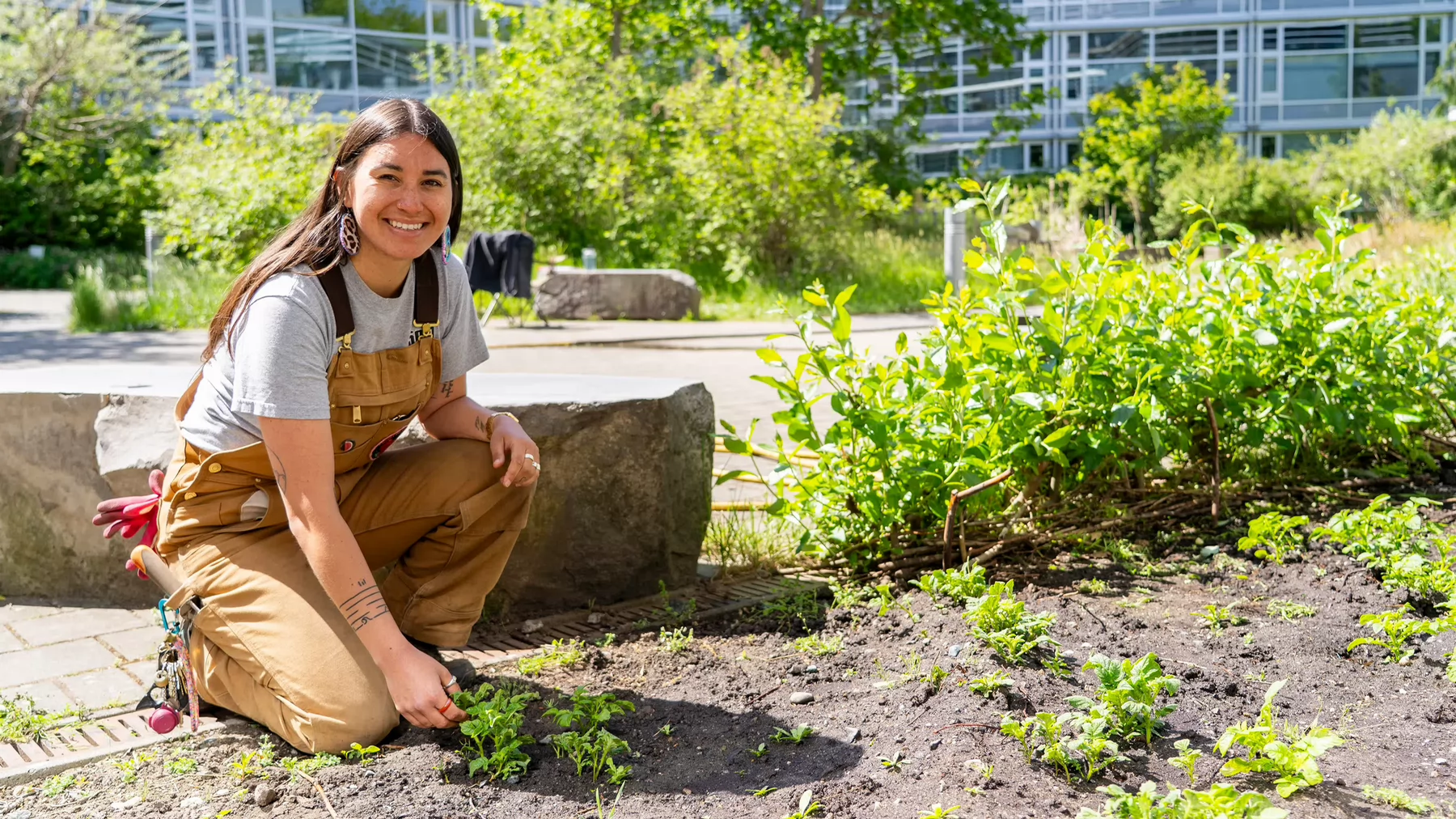 Loreisa Lepine kneels as she works in a plant bed in a courtyard on campus.
