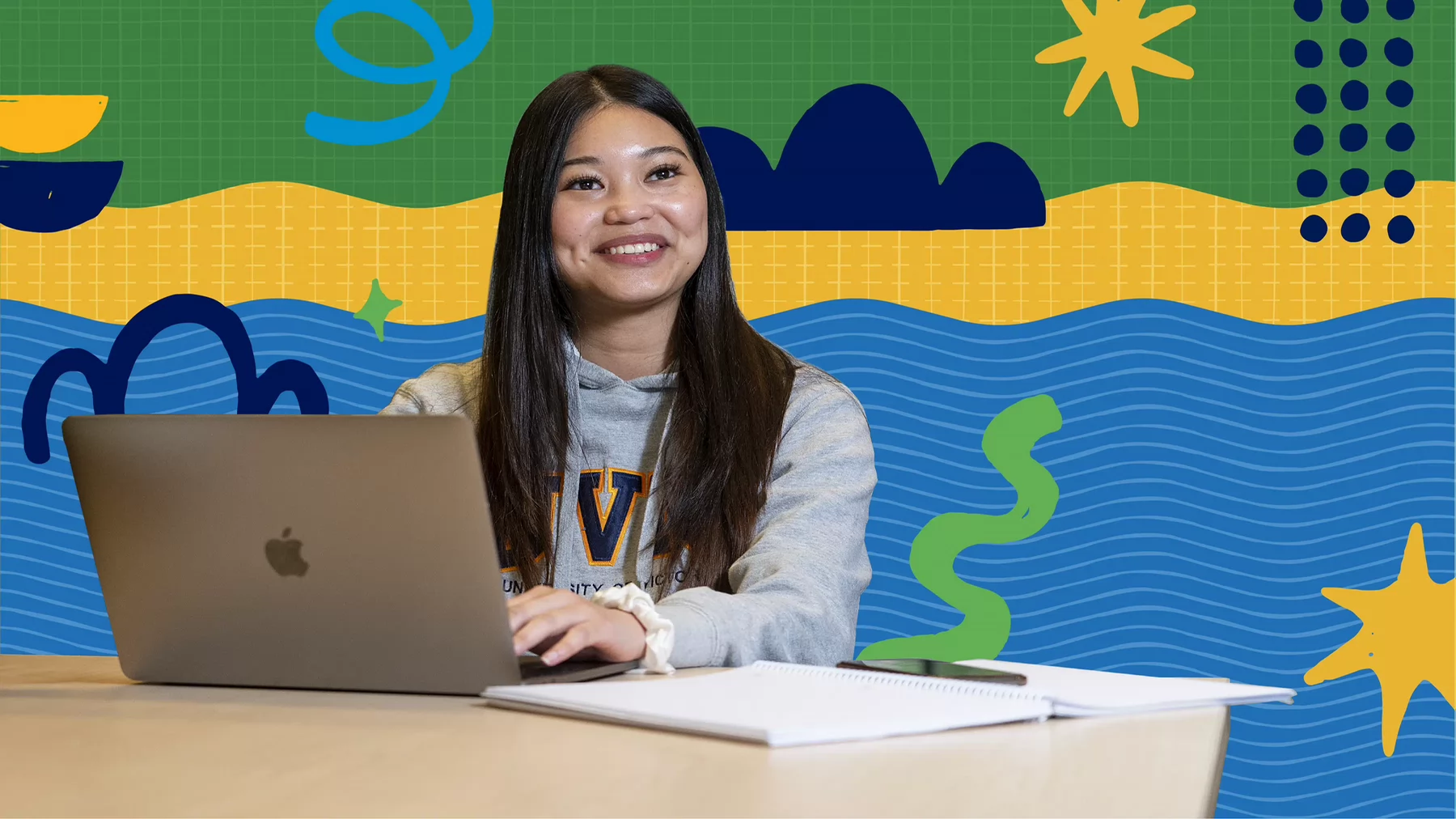A student sits at their open laptop, smiling and wearing a grey UVic branded sweatshirt. The background is a bright and colourful graphic illustration design.