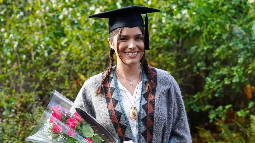 A new graduate smiling and holding a bouquet of flowers.