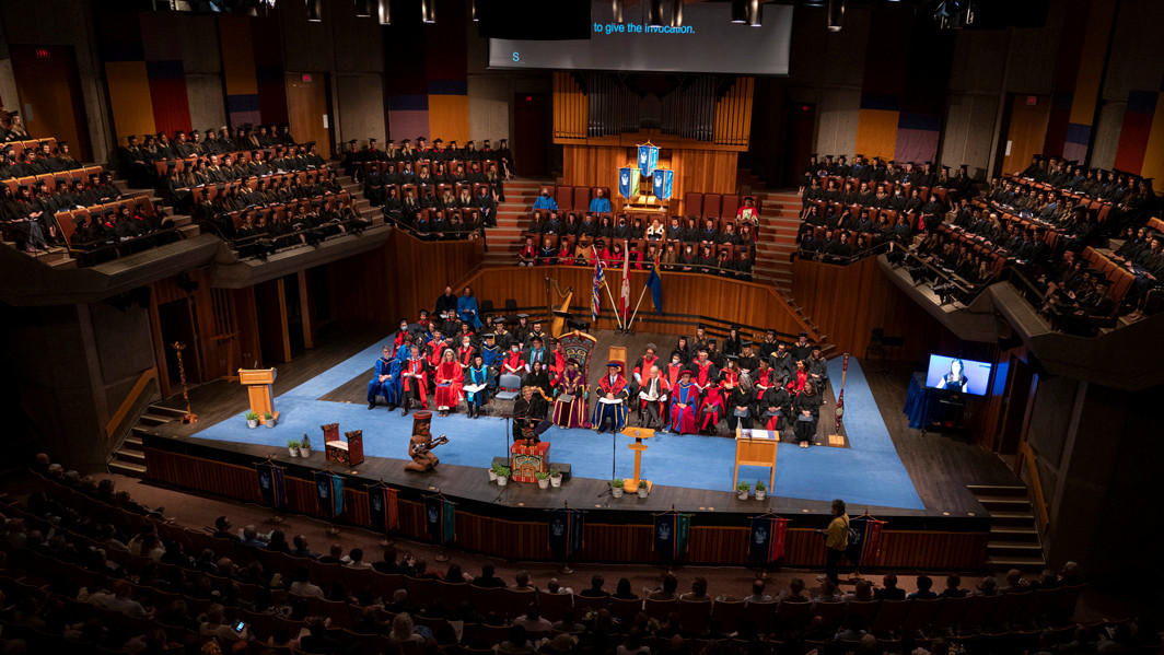 A wide-angle view of a graduation ceremony taking place in a large auditorium.