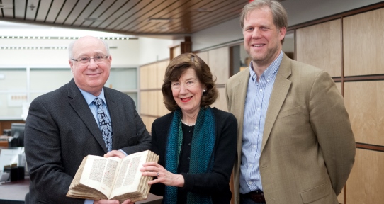 University Librarian Jonathan Bengtson is standing next to Brian Pollick and his wife Heather Lindstedt, who are holding an early Latin manuscript, the Codex Lindstedt. 