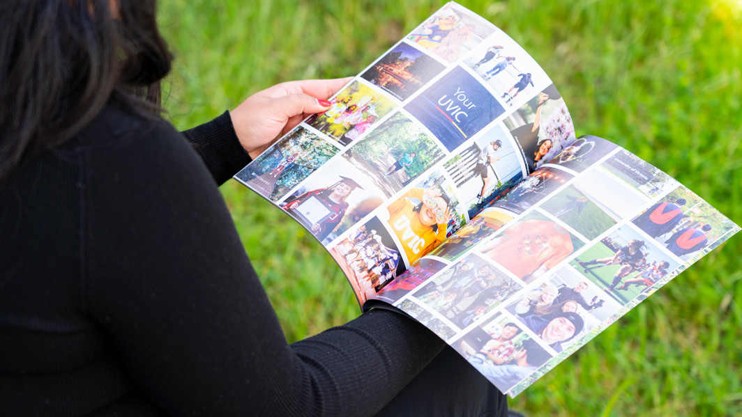 A person is holding and looking through a photo-filled graduation book. The book contains various images, including graduation pictures, group activities, and events.