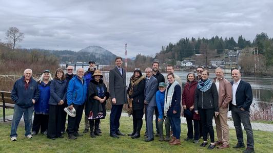 Group picture of nineteen people on the edge of the Cowichan Riven in British Columbia, including Premier David Eby and Cowichan Tribes Chief Cindy Daniels, Honorable Minister Nathan Cullen and Aaron Stone, chair of the Cowichan Valley Regional District.