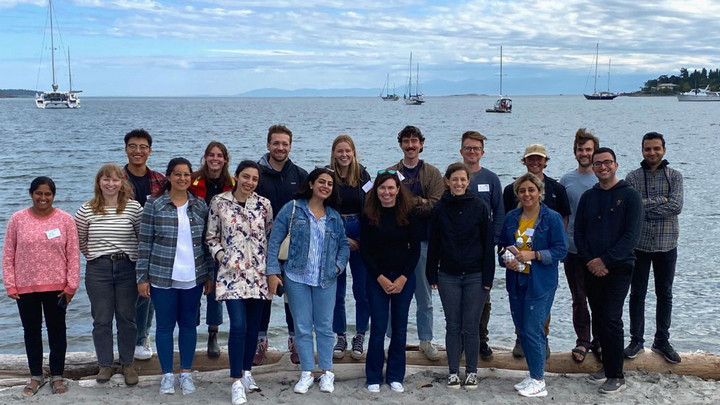 A group of students and their professor standing on the beach at Cadboro Bay