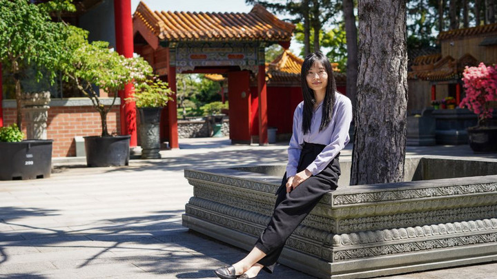 A woman in a purple shirt sits in a courtyard of a buddhist building