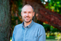 Portrait image of Dr. Felix Pretis on campus, wearing a blue button down shirt and standing in front of trees.