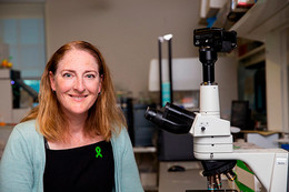 University of Victoria microbiologist, Caroline Cameron sits beside a microscope in a lab. 