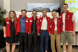 Six people stand together wearing red vests. They stand together in front of two presentation poster boards.