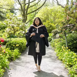A graduating student walks down a path in their regalia.