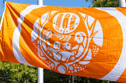 The National Centre for Truth and Reconciliation Survivors’ Flag is displayed. The flag is predominantly orange with white artwork depicting feathers, children. 