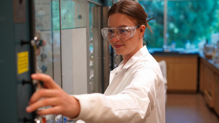 A student using lab equipment wearing lab coat and safety goggles