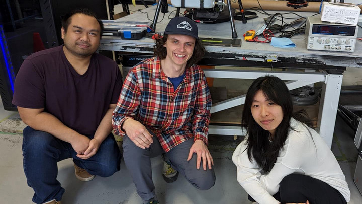 Three CfAR co-op students sit in front of model drone