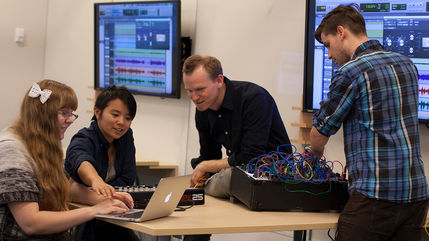 Three students work on laptops and sound mixing desks with professor Kirk McNally