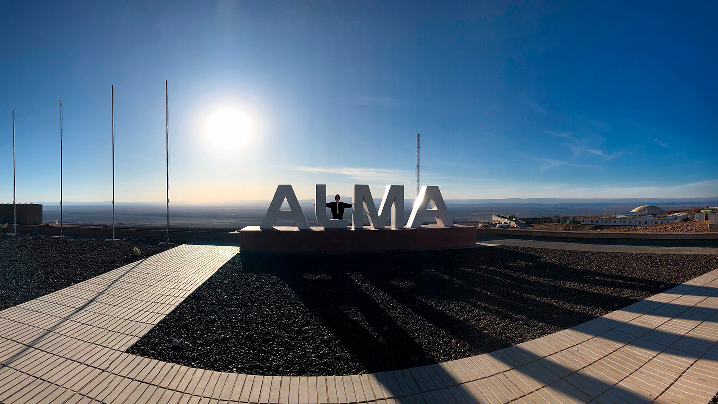 PhD student Jess Speedie stand in large ALMA logo sculpture