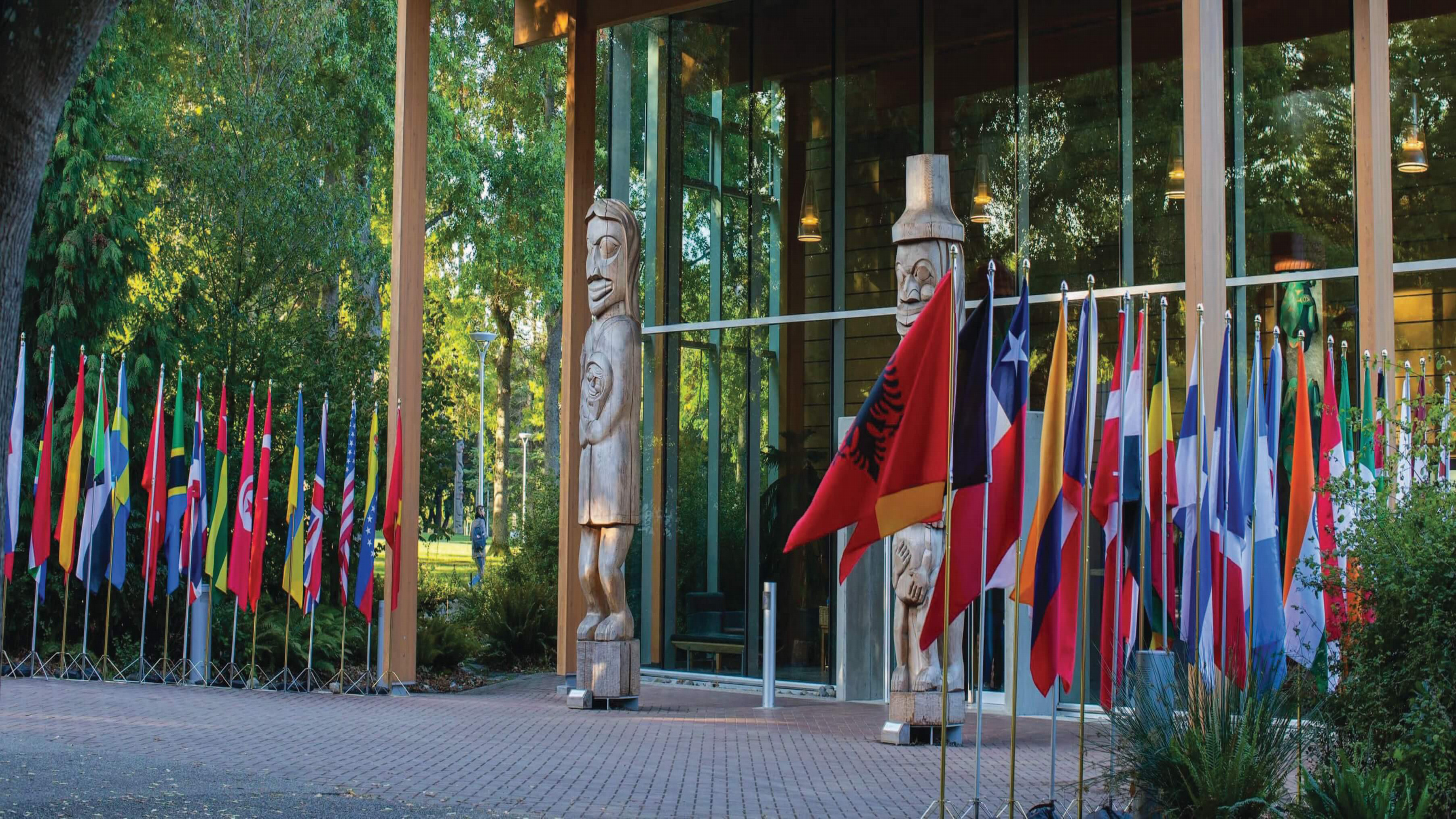 Photo of the entrance of UVic's First Peoples House with multiple countries flags lined up for a consular delegation visit