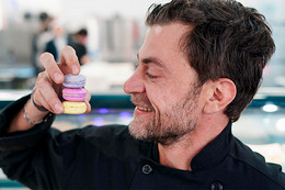 Man smiling while looking at a stack of three macarons he's holding in his hand