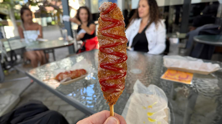 A hand holding up a deep-fried corndog covered in ketchup.