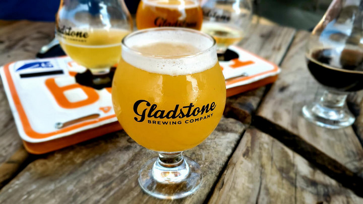 Glass of beer that says Gladstone brewing on it, among four other glasses of beer on a wooden table. 