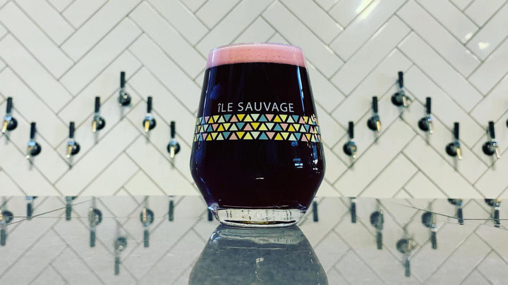 Glass of beer that says Ile Sauvage on a counter in front of beer taps.