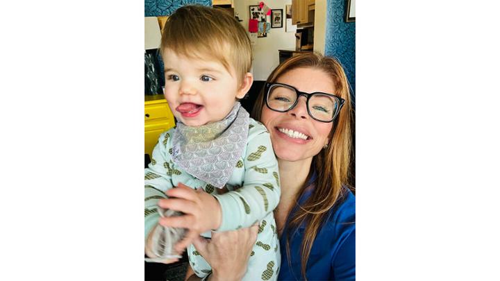 Women wearing glasses, smiling while holding toddler. 
