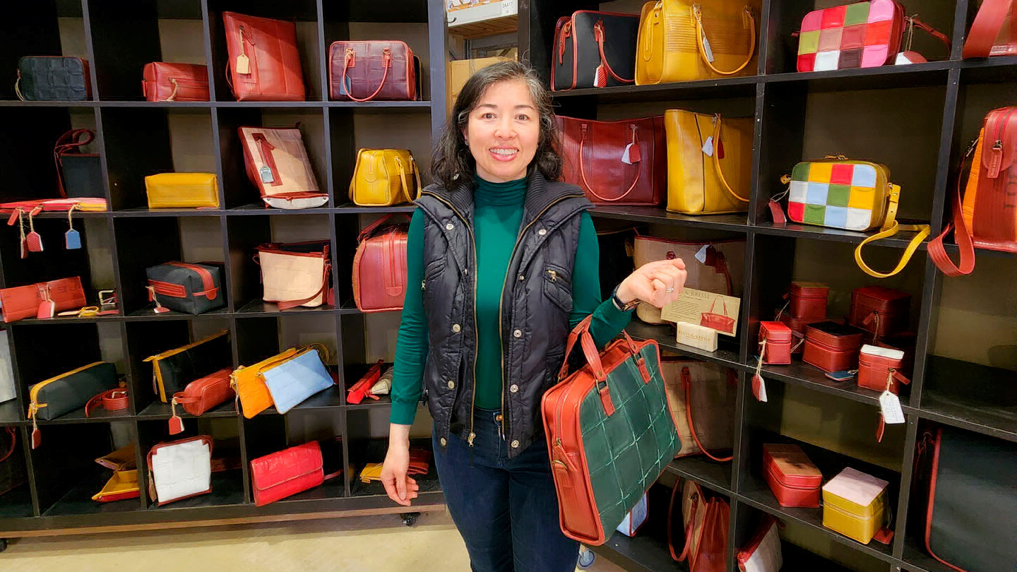 A woman stands in a shop with purses on display.