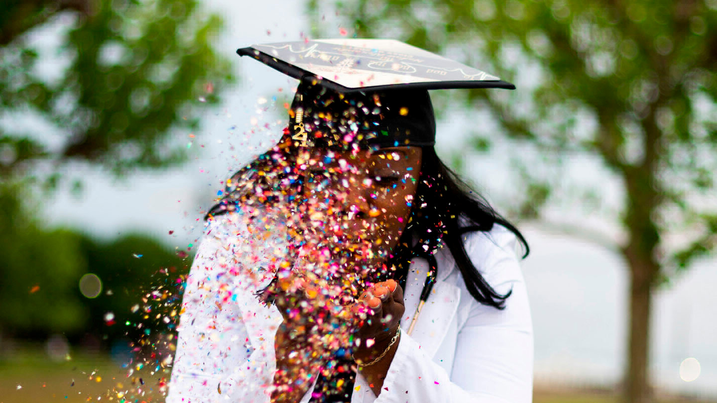A person wearing a graduation cap and gown throws confetti up in the air.