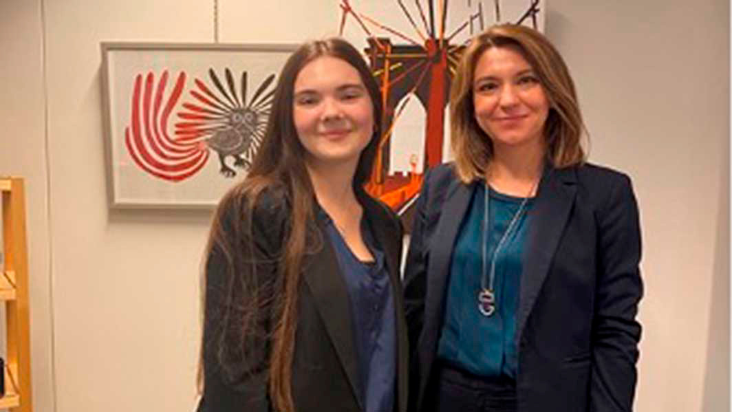 A student stands with their employer in front of some artwork.