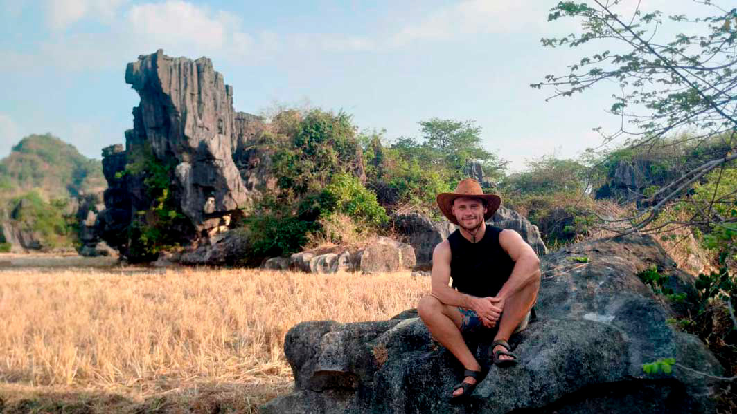 A student sits on a rock in front of an open field.