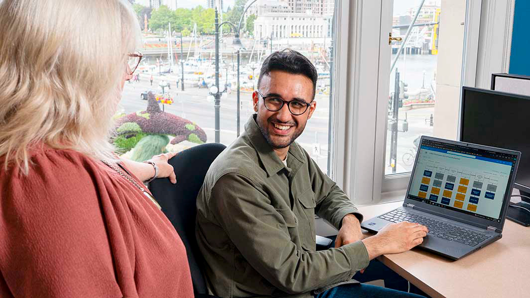 A student smiles at the employer while sitting at a desk in front of a window overlooking Victoria's Inner Harbour.