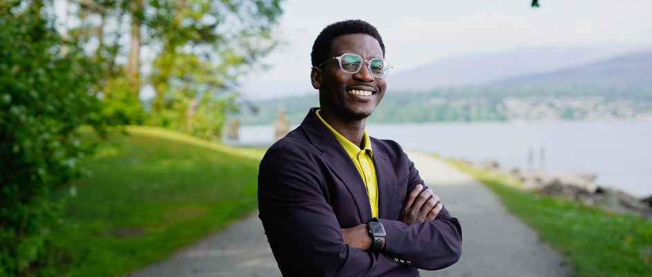 A man wearing glasses stands on a seaside path smiling