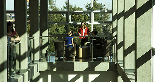 Two students standing in front of a large window overlooking the staircase.