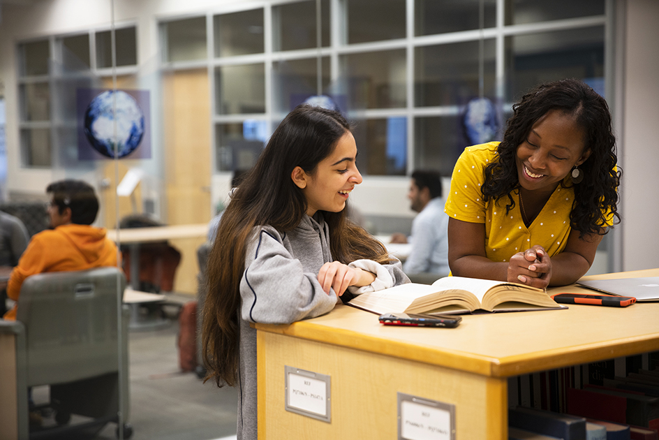 Two students chatting while reading a textbook in the library