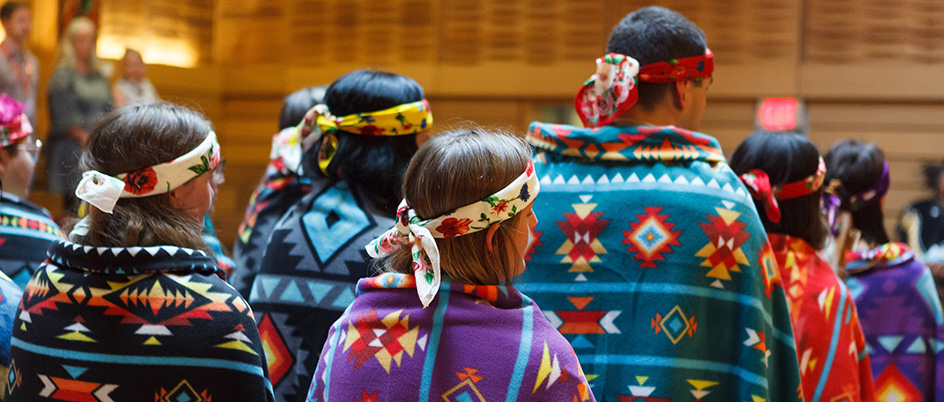 Several students face away from the camera, wearing colourful blankets wrapped around their shoulders. 