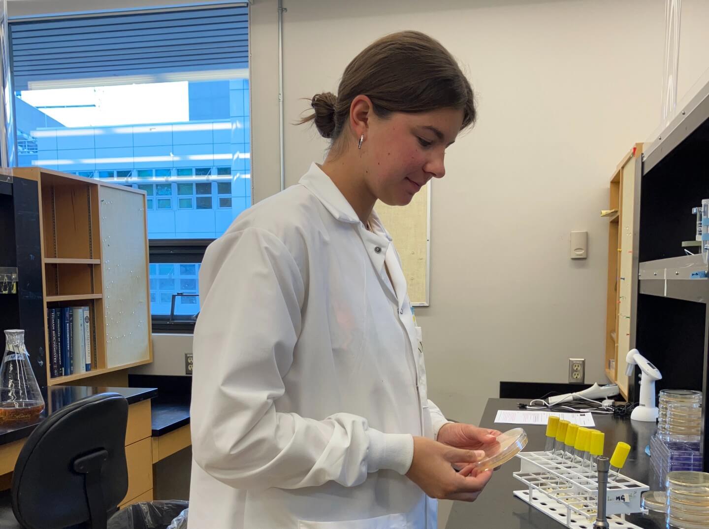 Elise Therrien in her lab coat, holding an agar plate at the lab bench