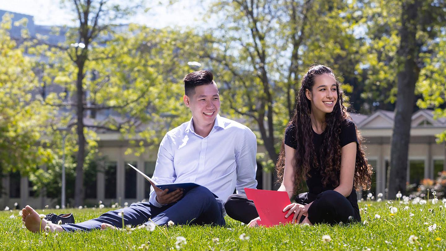 Two students sit in the grass at UVic campus.