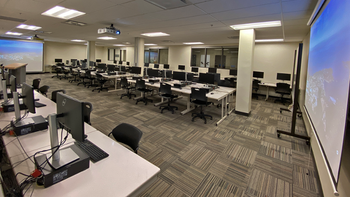 Large classroom with computer tables in centre, some computers around edge of room facing wall.